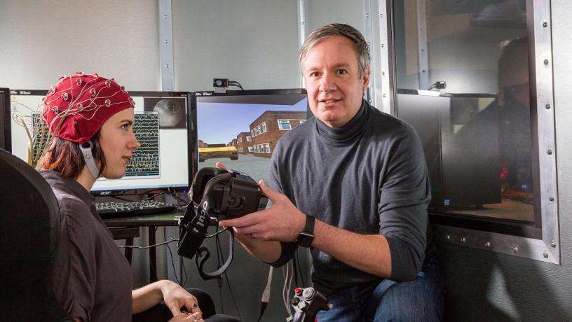 Prof. Paul Sajda holding VR glasses in his lab with research assistant Jennifer Cummings wearing electrodes.